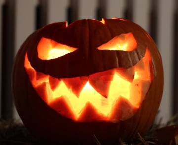 Close-up of a glowing, carved jack-o'-lantern pumpkin against a dark background.