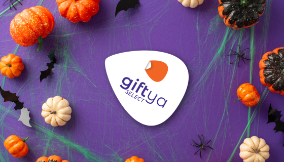 GiftYa Select logo badge surrounded by mini pumpkins, bats, and spiderwebs on a purple background.