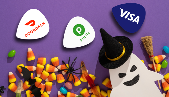 DoorDash, Publix, and Visa gift card logos displayed as guitar-pick badges among candy corn and a paper ghost decoration.